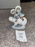 Front angled view of the Lladro Eskimo Riders porcelain figurine showing two children riding a white bear, placed on carpet with a 7-inch height note in front.