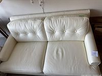 Front view of the white loveseat showing two seat cushions with button tufted back cushions and overall good condition with some visible signs of wear.