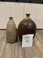 Two pottery vases shown together on a wood floor in front of white cabinets, one larger round and one smaller elongated.