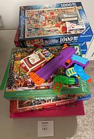Photo showing stacked Christmas-themed puzzles and three brightly colored water gun toys placed on top.