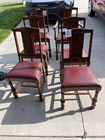 Eight wooden dining chairs arranged outdoors on pavement, showing both arm and armless types with burgundy cushions.