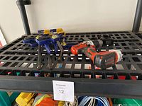 Black & Decker cordless drill and five Irwin quick-grip clamps on black shelf surface