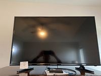 Full front view of the Insignia TV on a table with a remote, booklet, and cable in front, showing the screen and stand.