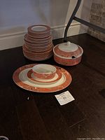 Stacked dinnerware plates with gravy boat and soup tureen on hardwood floor