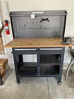 Front view of assembled Maximum workbench showing pegboard back, wood top, lower shelf and caster wheels