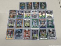 View of 23 football cards arranged in 3 rows on a white surface, showcasing holographic and prismatic finishes