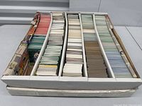 Top view photo of a large box filled with thousands of sports cards sorted in five rows by color and type.