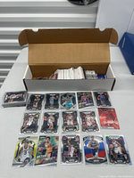 Open box filled with basketball cards, with 18 cards laid out in front showing a variety of players and card designs.