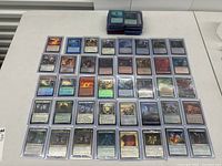 Spread of Magic The Gathering cards on a white table, showing multiple rows of holographic and non-holographic cards in protective sleeves.