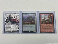 Three holographic Magic The Gathering cards in protective sleeves: Ezio Auditore da Firenze, Ygra, Eater of All, Ragavan, Nimble Pilferer.