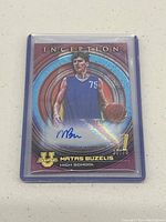 Photo of front side of Matas Buzelis signed basketball card with holographic circular design and autograph in blue ink. Serial number 30/75 visible in gold print.