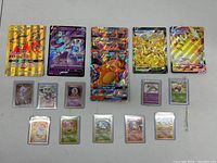 Full spread of Pokémon cards, including large and small cards inside hard plastic sleeves, showing Charizard GX cards, Pikachu V and Pikachu VMAX cards, and smaller vintage cards.