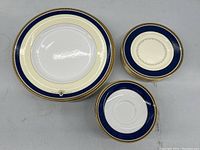 Stack of Royal Doulton plates showing dinner, luncheon, and bread and butter plates with cobalt blue, pale buttercream and gold patterning.