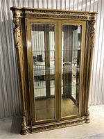 Front view of vintage gilt wood display cabinet with gold finish, two glass doors, and detailed carved columns.