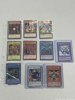 Photo showing all 10 holographic Yu-Gi-Oh! cards arranged in two rows of five, all sleeved and laid flat on a white surface.