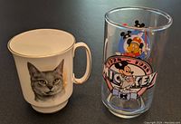 Photo of a fine bone china mug with a detailed cat image and a clear glass with vintage Mickey Mouse graphics