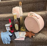 Photo of all items arranged on carpeted stairs showing all lot pieces including the pink cosmetic case, various bottles, sachets, and bath accessories.