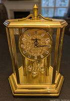 Front view of Birks quartz mantle clock with gold frame and glass panels showcasing the clock face and pendulum balls.