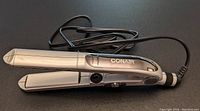 Silver Conair ceramic flat iron with a power cord and control buttons.