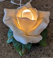 Top close-up view of the white rose lamp illuminated, showing detailed petals and green leaves at base.
