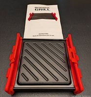 Photo showing the smaller 6x6 inch microwave grill with instruction manual on a dark surface.