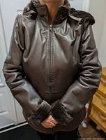 Front view of brown leather winter coat with faux fur lining, zipped up and showing hood down and fur cuffs.