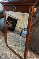 Full view of the large beveled mirror standing on carpet showing top decorative molding and reflection.