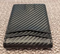Black leather billfold wallet with textured carbon fiber-like pattern shown front-facing, displaying two card slots on one side.