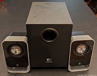 Front view showing the subwoofer and two satellite speakers on a table, with visible Logitech logos and a bass port on the subwoofer.