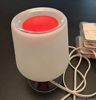 White frosted glass PartyLite SentGlow warmer plugged in with a red wax melt inside the removable dish, shown glowing.