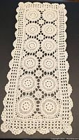 Rectangular crochet doily with circular patterns and edged scallops on dark background