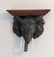 Front view of elephant head wall shelf with wooden top showing intricate sculpted features and tusks