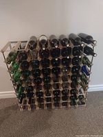 Front view of a large wood and metal wine rack partially filled with empty wine bottles. The rack has multiple rows and columns holding individual bottles horizontally.