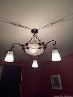 Installed view from below showing central frosted glass bowl suspended by chain and three downward-facing frosted shades