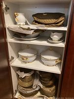 Shelved assortment of stacked white china pieces wrapped in protective gold and cream cloth, including plates, bowls, gravy boats, and additional items.