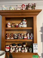 Front view of multiple ceramic Christmas-themed salt and pepper shakers and figurines arranged on wooden shelf including snowmen, Santa, gingerbread men, candy canes, and others.