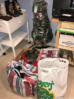 Wrapped artificial Christmas tree and bags of decorations on floor near furniture