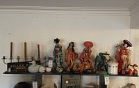 Full shelf showing various Oriental dolls, candelabra, bowls, and figurines.