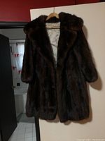 Front view of the dark brown mink fur coat hanging on a wooden hanger against a white background.