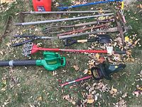 Full view of garden tools laid on lawn including Jerry can, hand tools, blower, and trimmer.