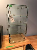 Front view of a four-shelf glass display case on a wooden table showing glass shelves and metal fasteners.