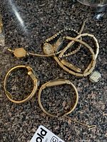Photo showing seven gold fill wristwatches arranged on a granite countertop, including various band styles and one watch without a strap.