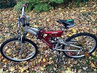 Full side view of the red and silver Infinity Cork mountain bike with Velo seat, showing the overall condition, frame, and tires flat on the leaf-covered ground.