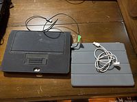 Apple iPad and Microsoft Surface tablets with their cases and charging cables on a wooden surface.