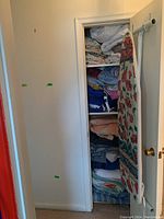Closet door open showing shelves packed with folded linens and blankets, with ironing board leaning inside closet.