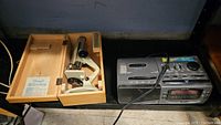 Photo showing the microscope in wooden box and Sanyo digital clock radio cassette tape player side by side on a shelf.