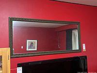 Full view of the mirror mounted on a red wall above a TV, showing the full rectangular shape and frame edges.