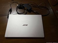 Closed silver Acer Swift 3 laptop with top lid showing Acer logo and attached power adapter on wooden surface.