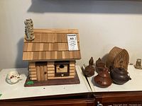 Wide view of wooden model house with chimney and assorted pottery items including teapots, pottery birds, and small teacup with saucer