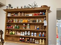 Wide view of a wooden shelf filled with multiple ceramic salt and pepper shakers in varying characters, colors, and sizes.